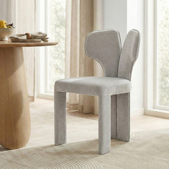 Two light gray upholstered chairs by a wooden dining table in bright room