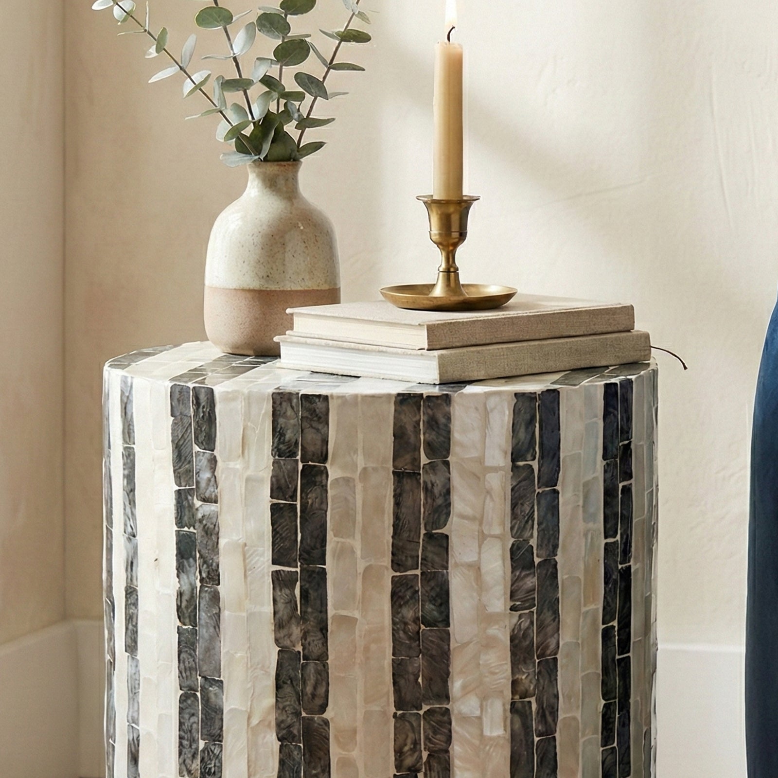 Close crop of tiled side table with vase, books, and candle in a home corner