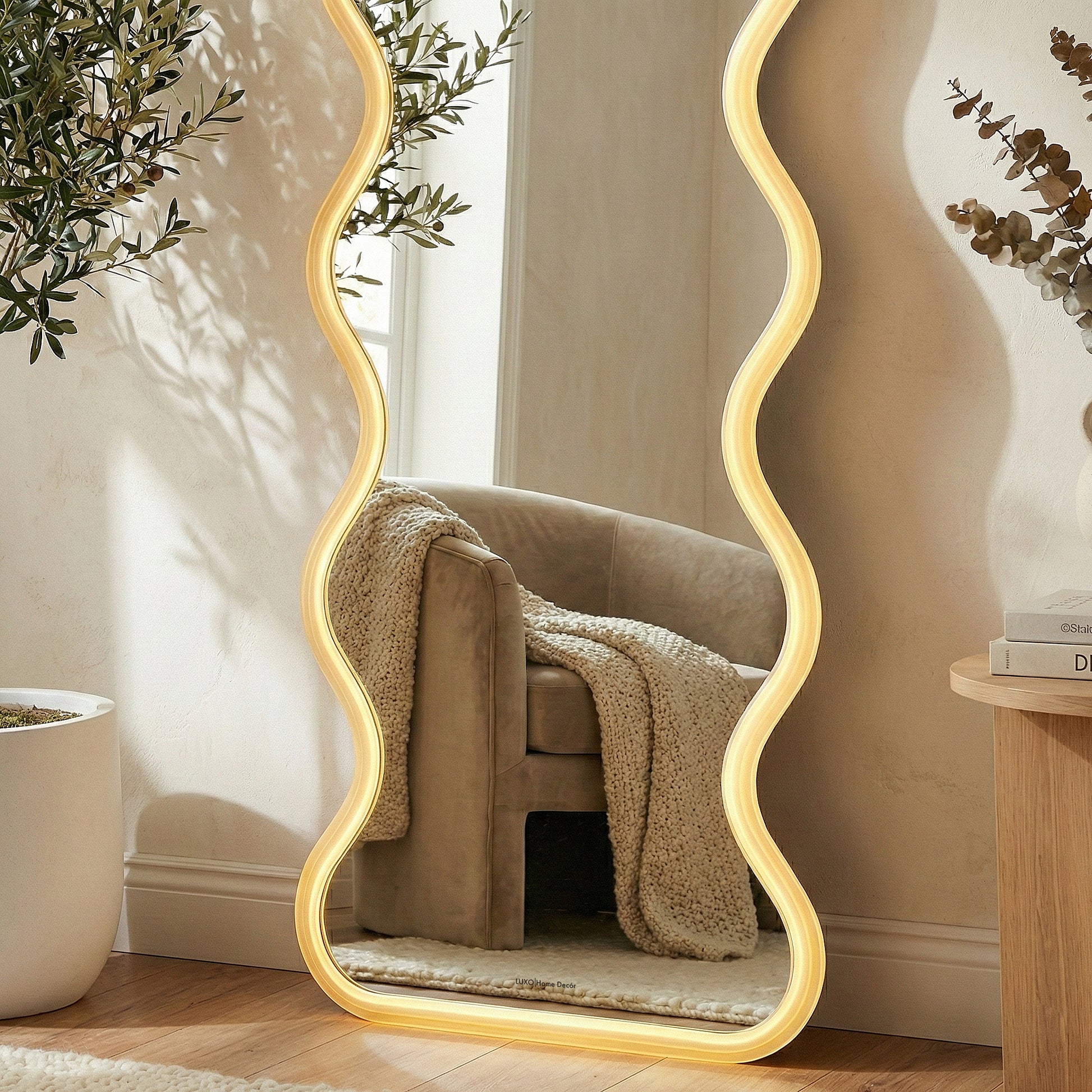 Full-length wavy LED mirror in a modern room next to an armchair and decorative items