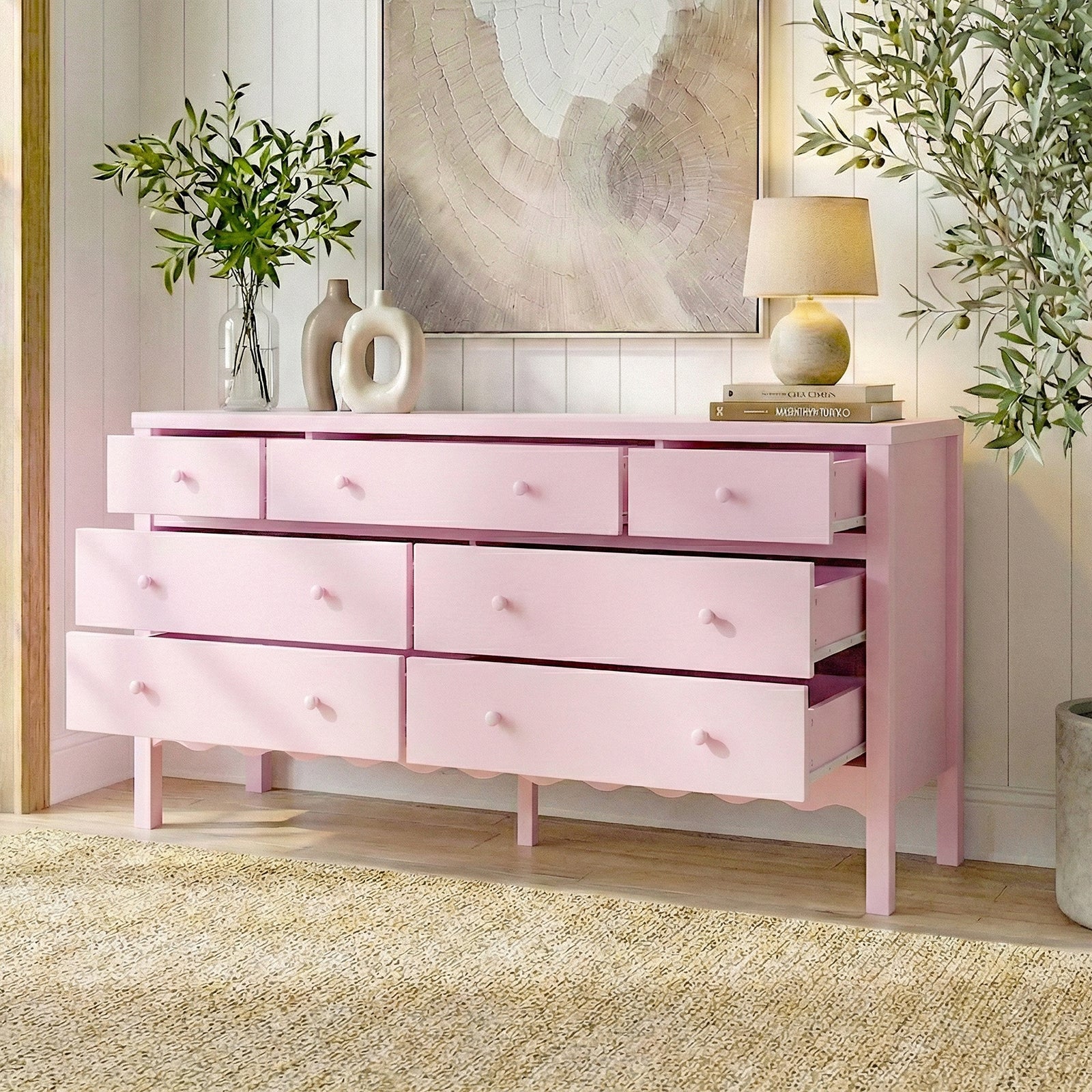 Pink dresser with nine drawers styled with vases, lamp, and plants