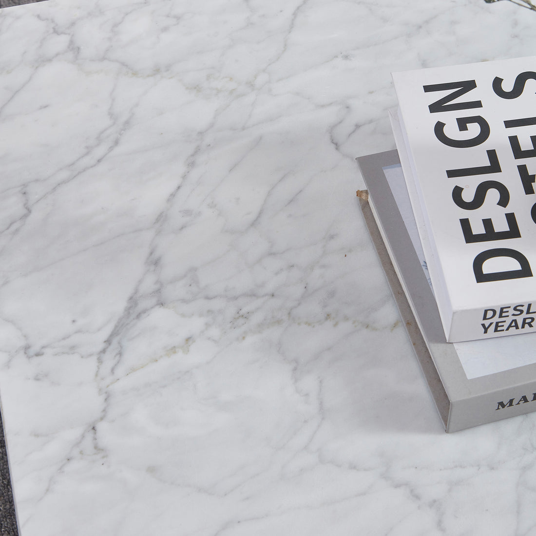 Solene 100cm Coffee Table in Carrara on a white marble surface, featuring a small stack of hardcover books. The table showcases its elegant, authentic marble veining and sleek, low-profile design.