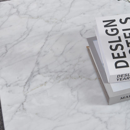 Solene 100cm Coffee Table in Carrara on a white marble surface, featuring a small stack of hardcover books. The table showcases its elegant, authentic marble veining and sleek, low-profile design.