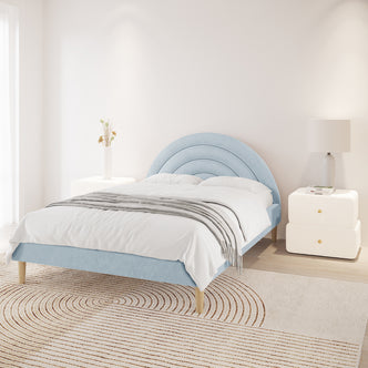 Estilla Velvet Rainbow Bed in Ice Blue, featuring a concentric semi-circle headboard, white linens, gray throw, and adjacent white side tables with a vase and lamp, in a sunlit, minimalist bedroom.