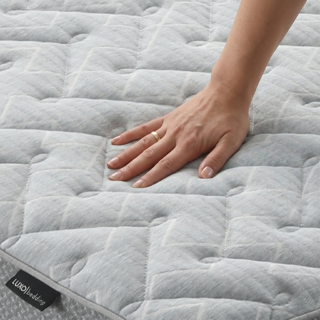 Hand pressing on quilted mattress surface to show softness
