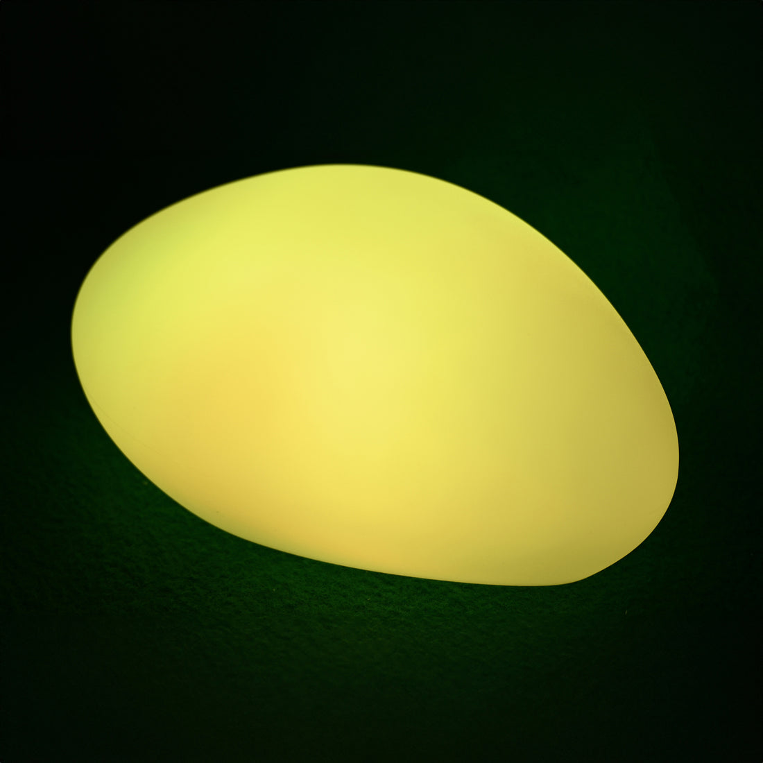 Solar Charging Outdoor LED Rock Light, a pebble-shaped object softly glowing with warm light, designed to blend into gardens, providing discreet, cordless illumination with a natural stone appearance.