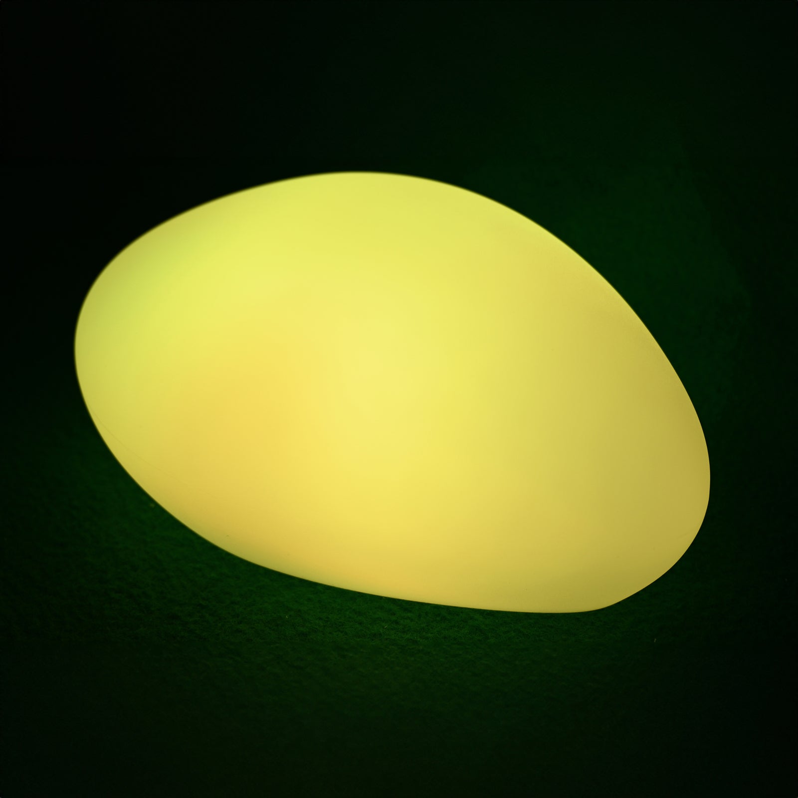 Solar Charging Outdoor LED Rock Light, a pebble-shaped object softly glowing with warm light, designed to blend into gardens, providing discreet, cordless illumination with a natural stone appearance.