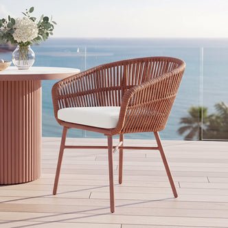 Marula Rope Outdoor Dining Chairs in Terracotta Set of 4 showcase woven rattan-style backs, slender metal legs, plush white cushions, and a terracotta pedestal table with blooms, offering stylish alfresco comfort.
