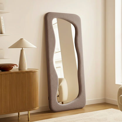 Sabrina 180cm Curved Full Length Mirror in Taupe Brown features a wavy, bouclé frame, leaning elegantly in a softly lit, modern-Scandi interior, reflecting a serene, stylish ambiance.