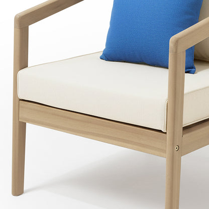 The Delva 4 Seater Hardwood Acacia Outdoor Sofa Set in Cream features a modern armchair with a light wood frame, off-white cushion, and a blue throw pillow, highlighting its stylish, comfortable design.