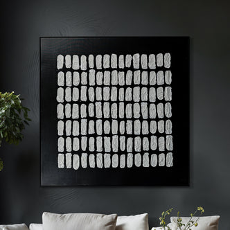 Elodie Framed Canvas Wall Art 105 x 105cm in Black, featuring a textured abstract grid of white brush-stroke marks, set against a modern living room backdrop with greenery accents.