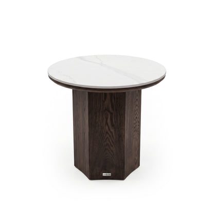 Round side table with a white marble top and dark geometric pedestal base on a white background