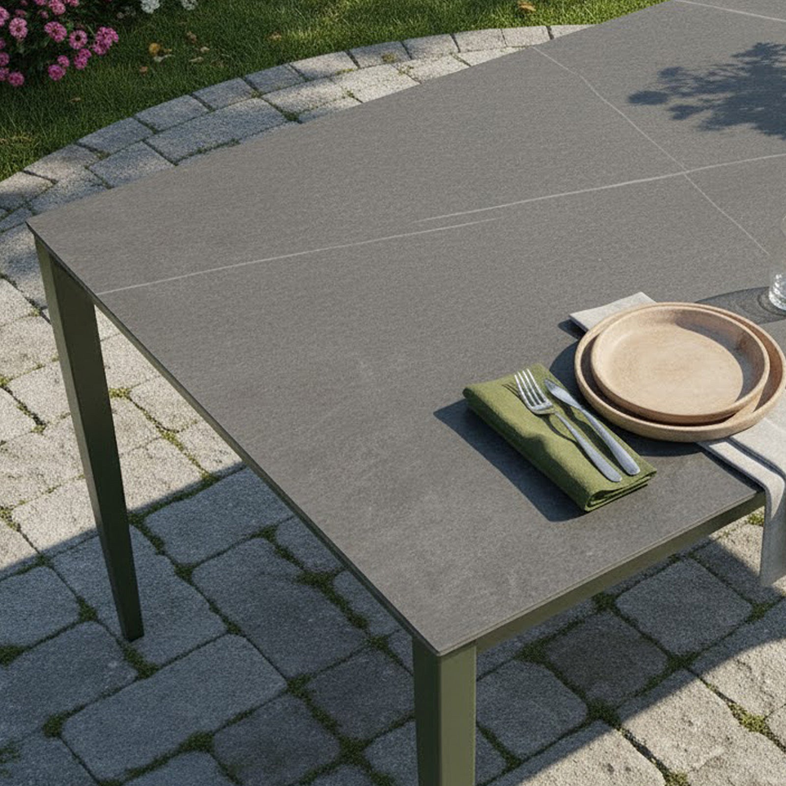 Cabria 9 Piece Sintered Stone Outdoor Dining Set in Green featuring a dark stone-like table with slim metal legs, adorned with a green napkin, cutlery, wooden plates, and a glass.