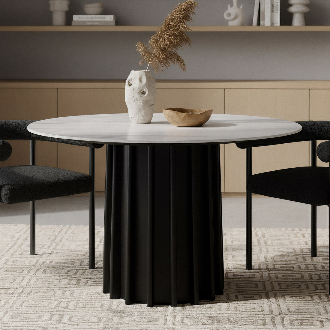 Gabi 120cm Marble Look Dining Table in Black features a white top and fluted black base. It is accented by a textured vase with pampas grass and a wooden bowl, flanked by black chairs.