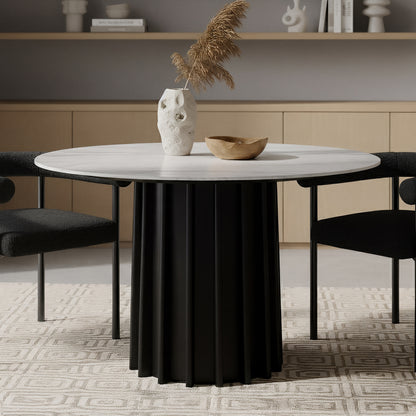 Gabi 120cm Marble Look Dining Table in Black features a white top and fluted black base. It is accented by a textured vase with pampas grass and a wooden bowl, flanked by black chairs.