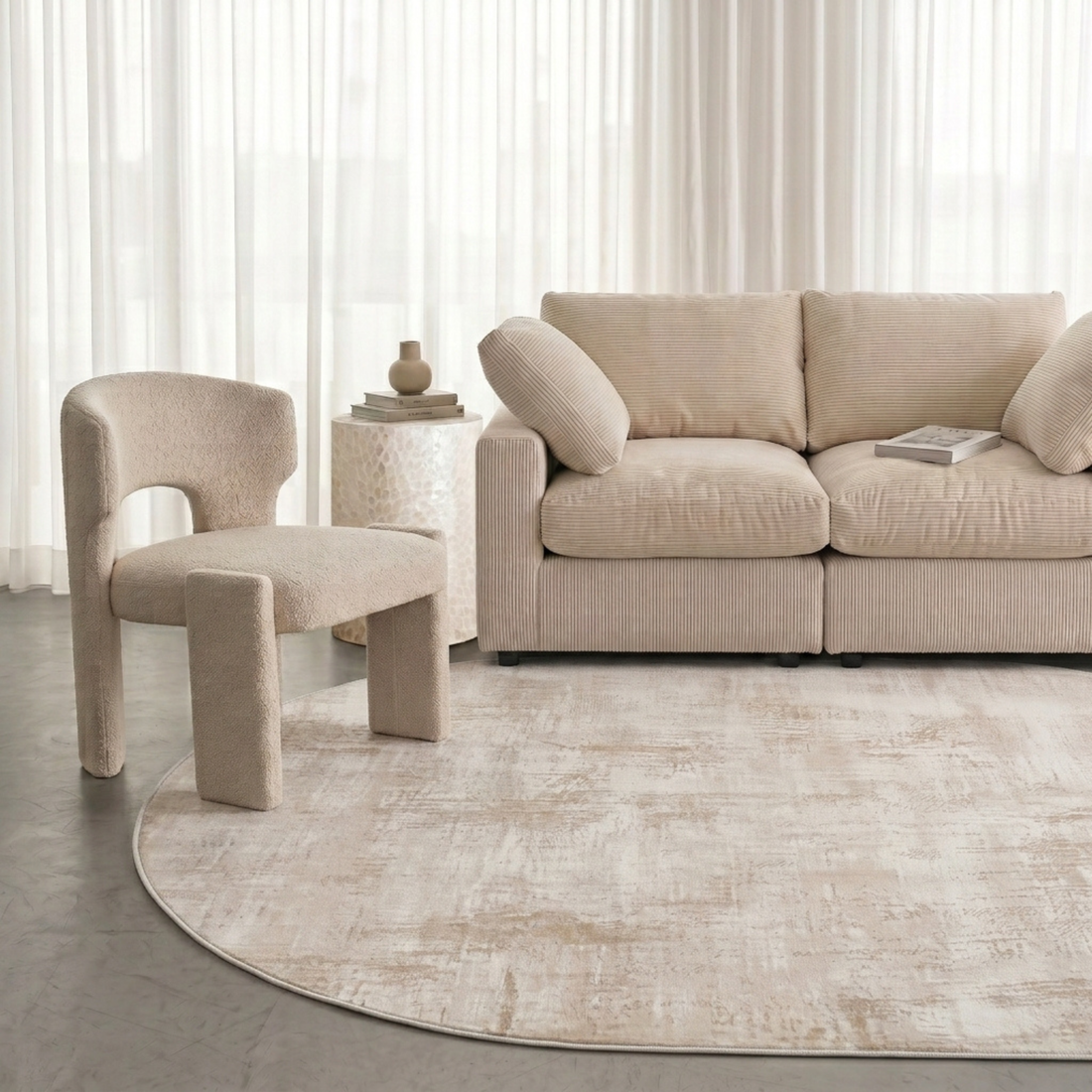 Oval beige rug displayed in a modern neutral living room with sofa, chair, and side table