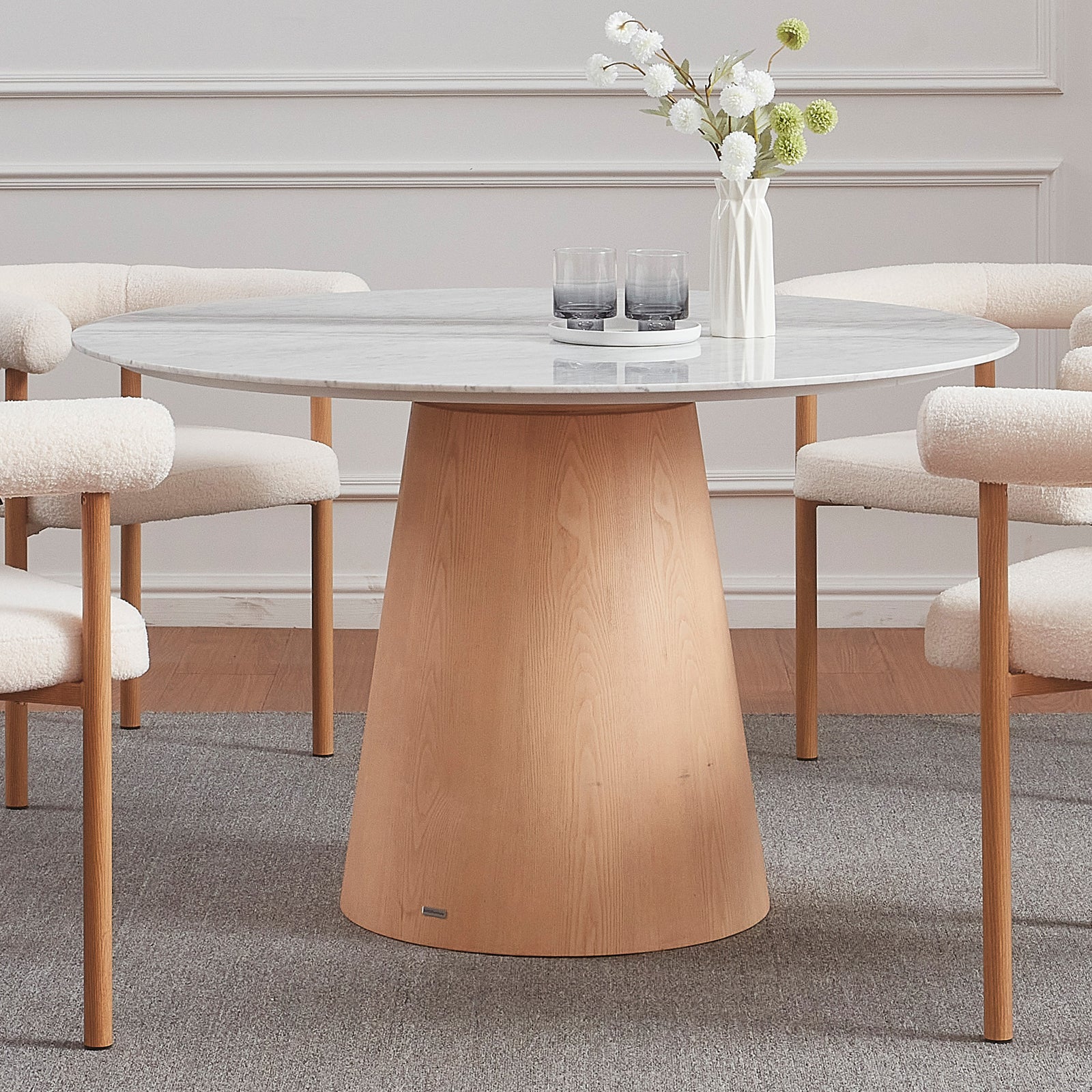 Dina 120cm Round Marble Dining Table in Carrara Natural with a pale gray marble top on an oak base, surrounded by four bouclé-upholstered chairs, accented by a vase and tray.