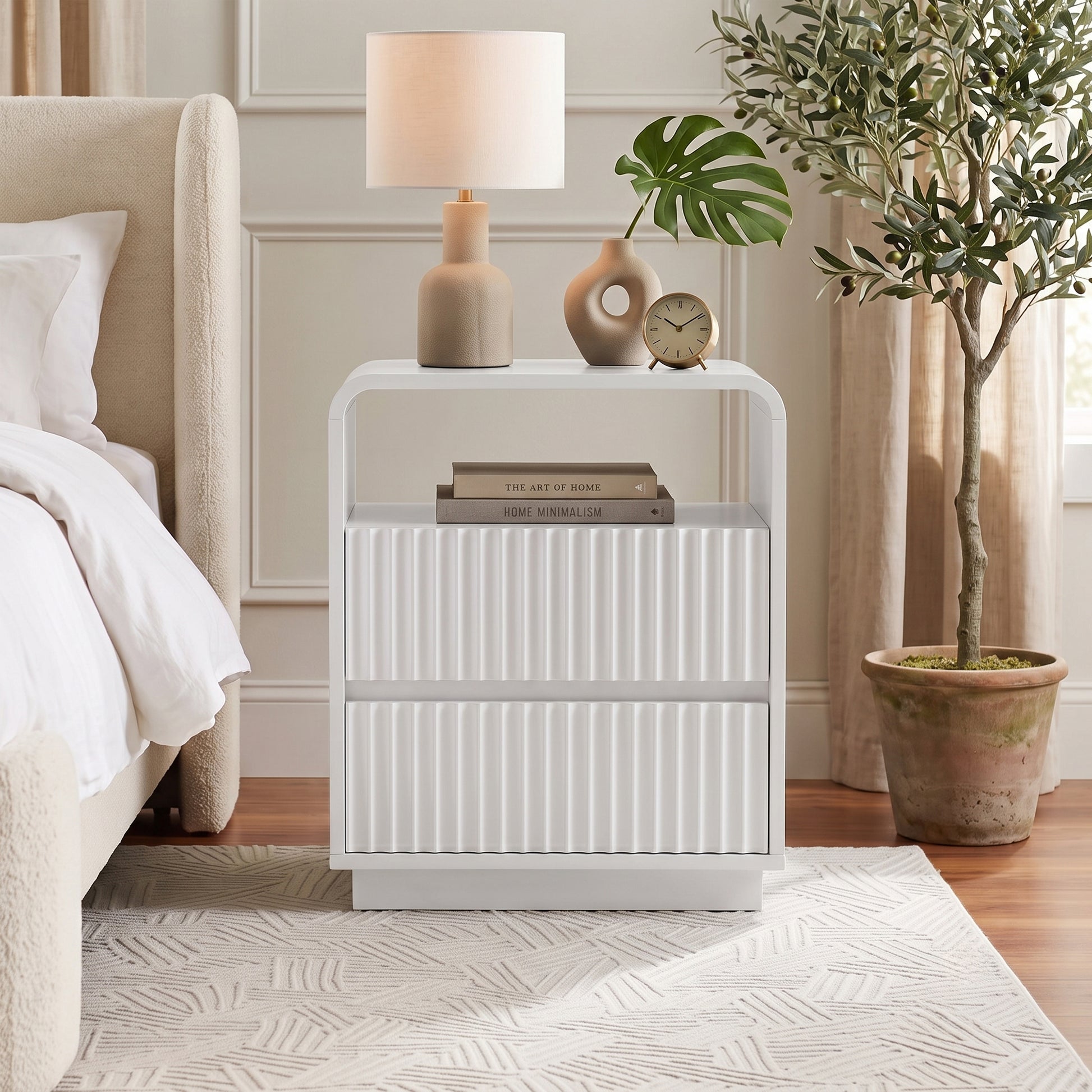 White nightstand styled in a modern bedroom next to a bed with decor items on top.