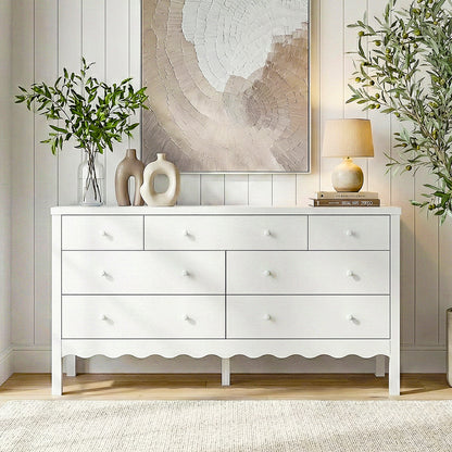 White nine-drawer dresser styled in a bright, contemporary living space against a paneled wall