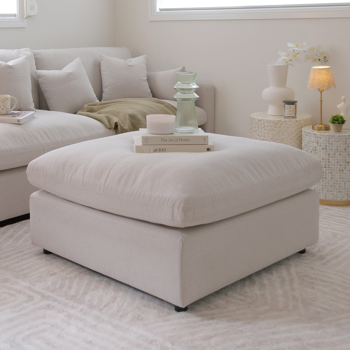 Large neutral ottoman in a bright, stylish living room with sectional sofa and decor