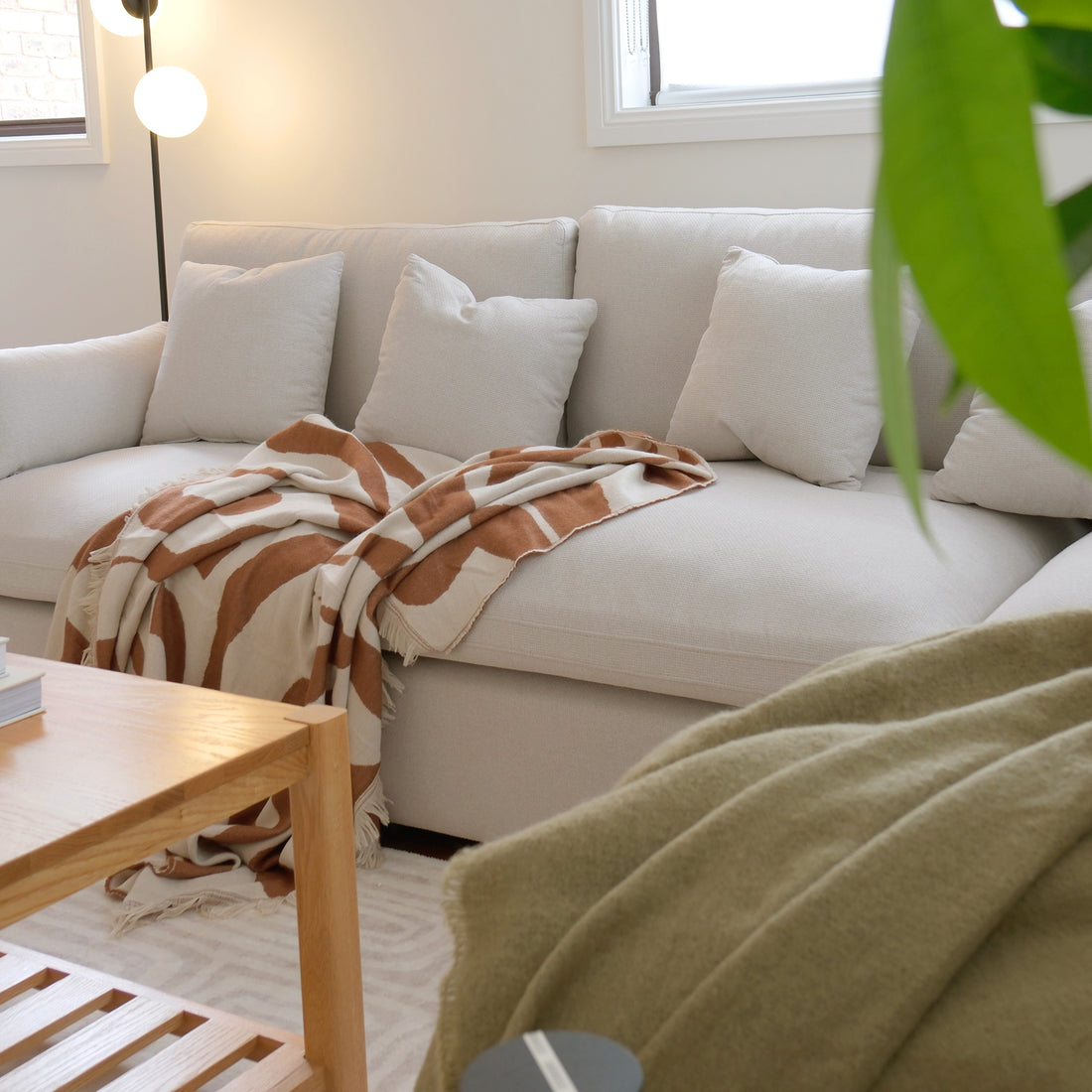 Light-colored sectional sofa in a bright living room with pillows and throw blanket