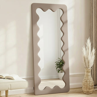 Serena 180cm Full Length Mirror in Taupe Brown with wavy-edged frame, styled with a bench, book, woven vase with dried grasses, and potted plant, creating a minimalist home decor vignette.