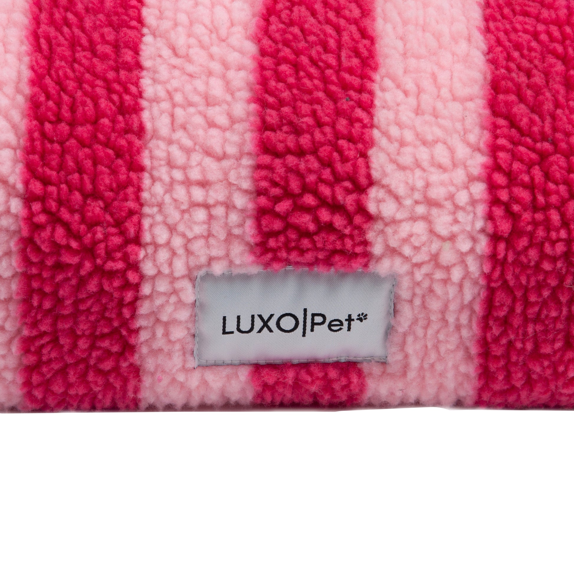 Close-up of pink and light pink striped plush fabric with 'LUXO|Pet' brand tag on a white background