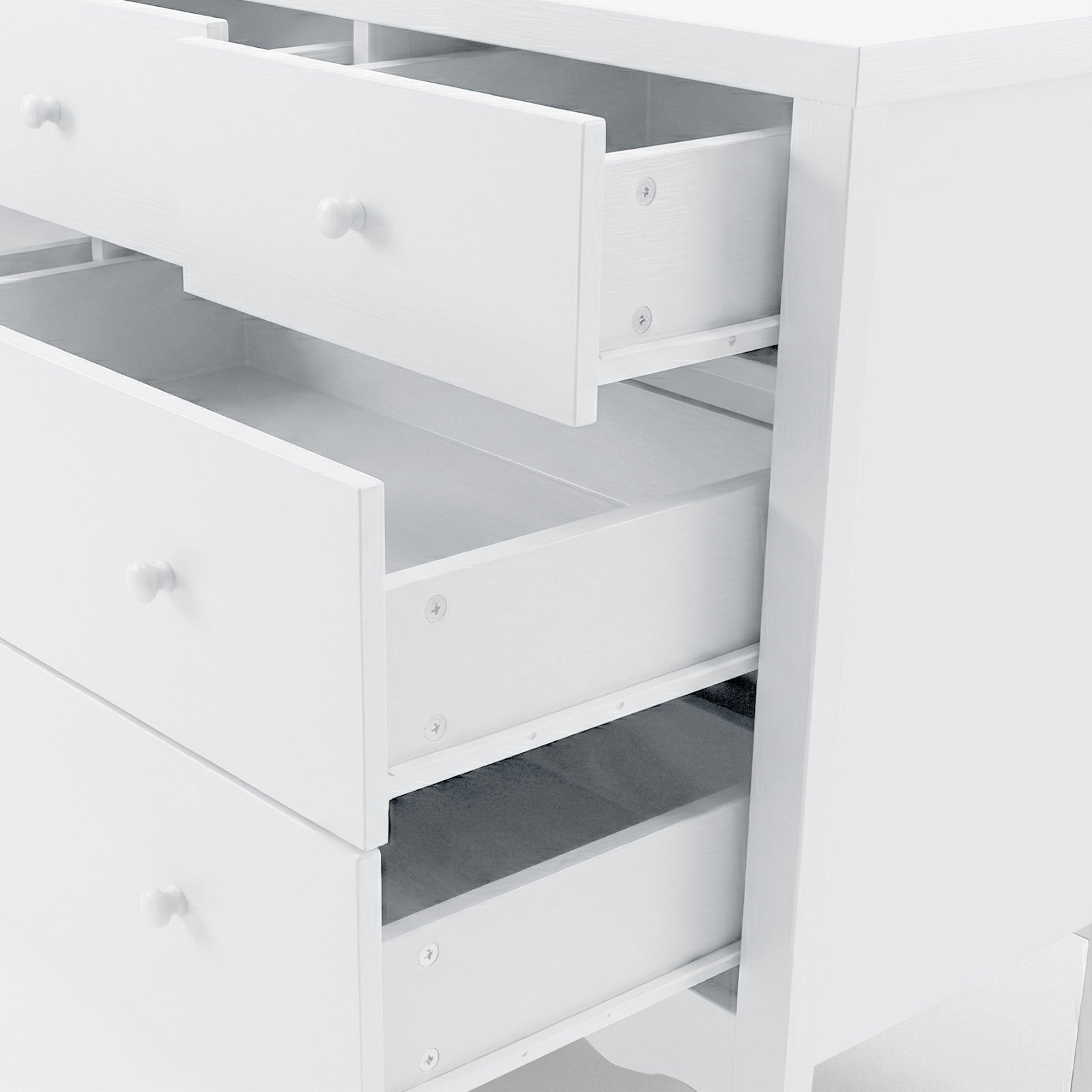 Angled, partial view of white chest of drawers with open drawers on white background