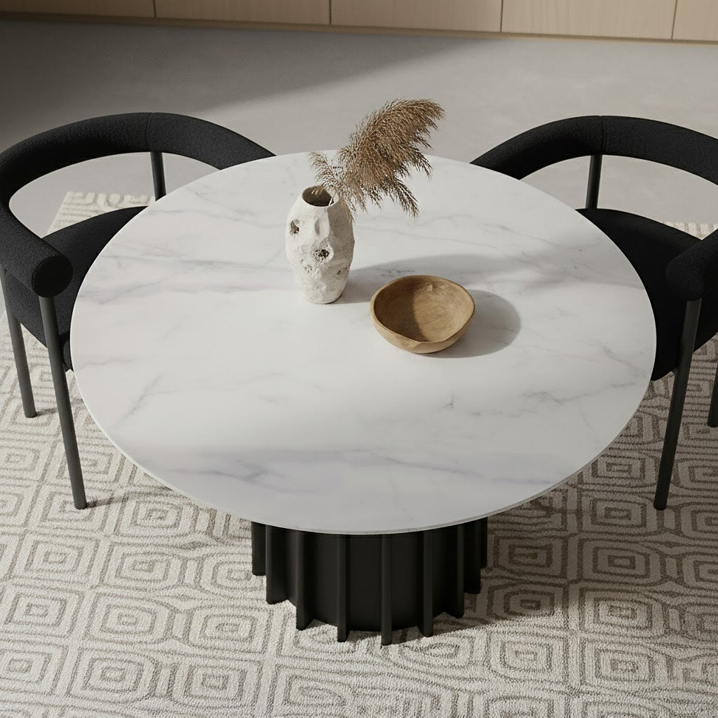 Gabi 120cm Marble Look Dining Table in Black with a round marble-look top and fluted base, styled with a ceramic vase of pampas grass and a wooden bowl, flanked by black chairs.