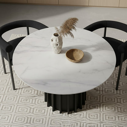 Gabi 120cm Marble Look Dining Table in Black with a round marble-look top and fluted base, styled with a ceramic vase of pampas grass and a wooden bowl, flanked by black chairs.