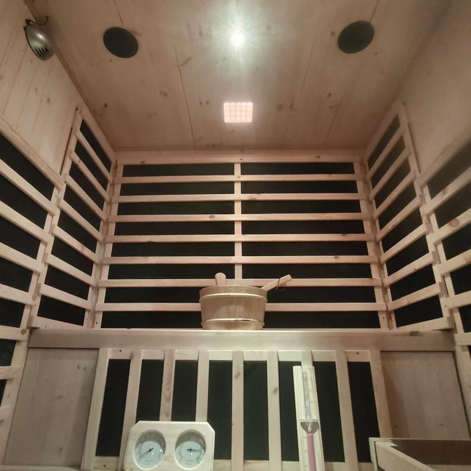 Luxo Kiima 3 Person Hybrid Finnish Outdoor Sauna in Natural features slatted wood walls, infrared panels, a bench with a wooden bucket and ladle, gauges, and a sand-timer, evoking a serene spa experience.