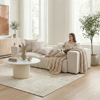 Beige L-shaped sectional sofa in a bright living room with a woman lounging