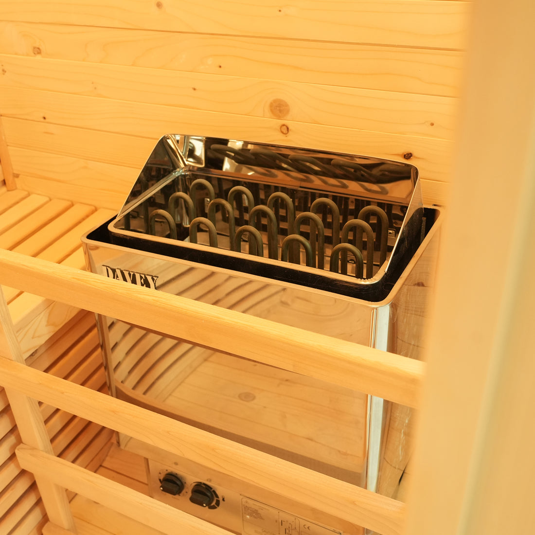 Kivi 3-Person Traditional Stove Finnish Indoor Home Sauna featuring a stainless steel Davey electric heater with U-shaped elements, surrounded by wooden guardrails and benches, inside a wooden-paneled sauna cabin.