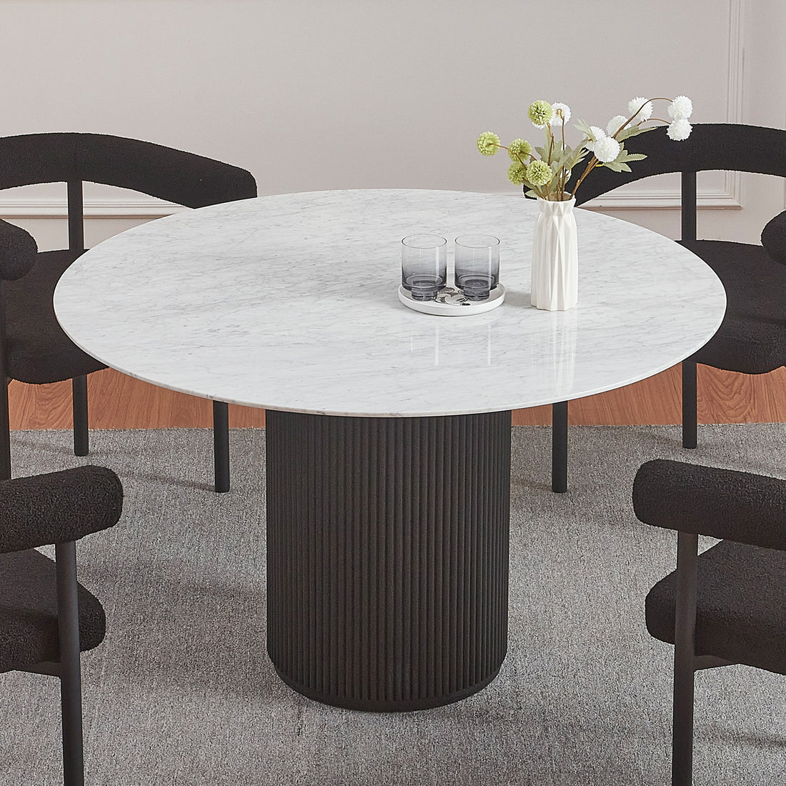 Gracie 120cm Round Marble Dining Table in Black with a fluted cylindrical base, topped with a small white vase and tray with glasses, surrounded by four low-back upholstered chairs.