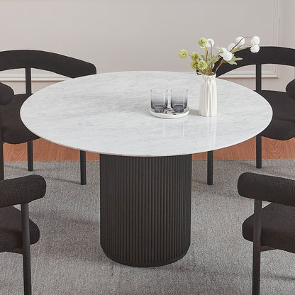 Gracie 120cm Round Marble Dining Table in Black with a fluted cylindrical base, topped with a small white vase and tray with glasses, surrounded by four low-back upholstered chairs.