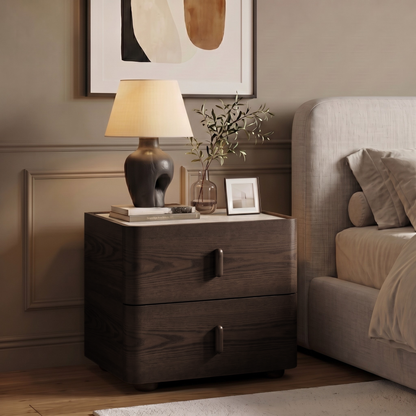 Dark wood nightstand styled beside a bed in a cozy bedroom with lamp, books, and decor.