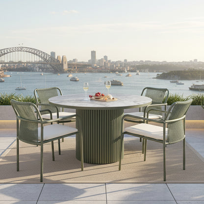 Evone 4 Seater Stone Outdoor Dining Table Set in Green with marble top, rope-back chairs, cheese board, and wine, set on a terrace with a harbor and bridge view.