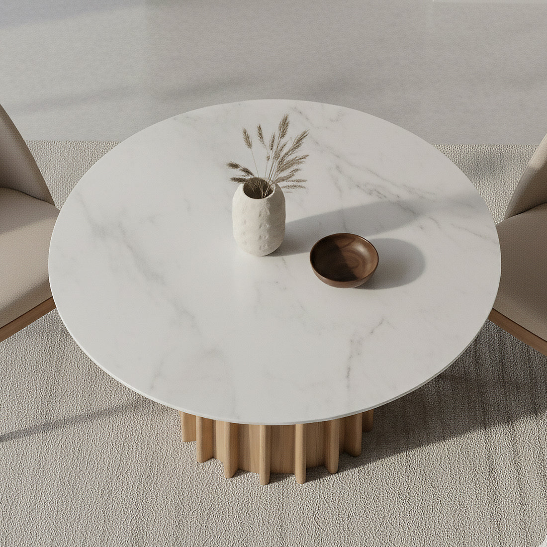 Gabi 120cm Marble Look Dining Table in Oak features a round, marble-like top with a sculptural fluted wooden base, adorned with a ceramic vase and shallow wooden bowl, set on a textured rug.