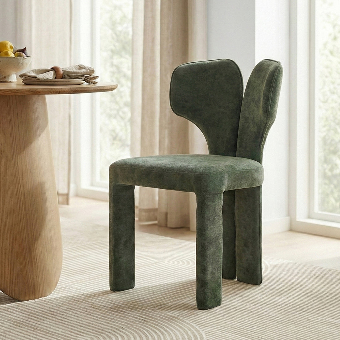 Green upholstered chair beside wooden table with fruit in bright room