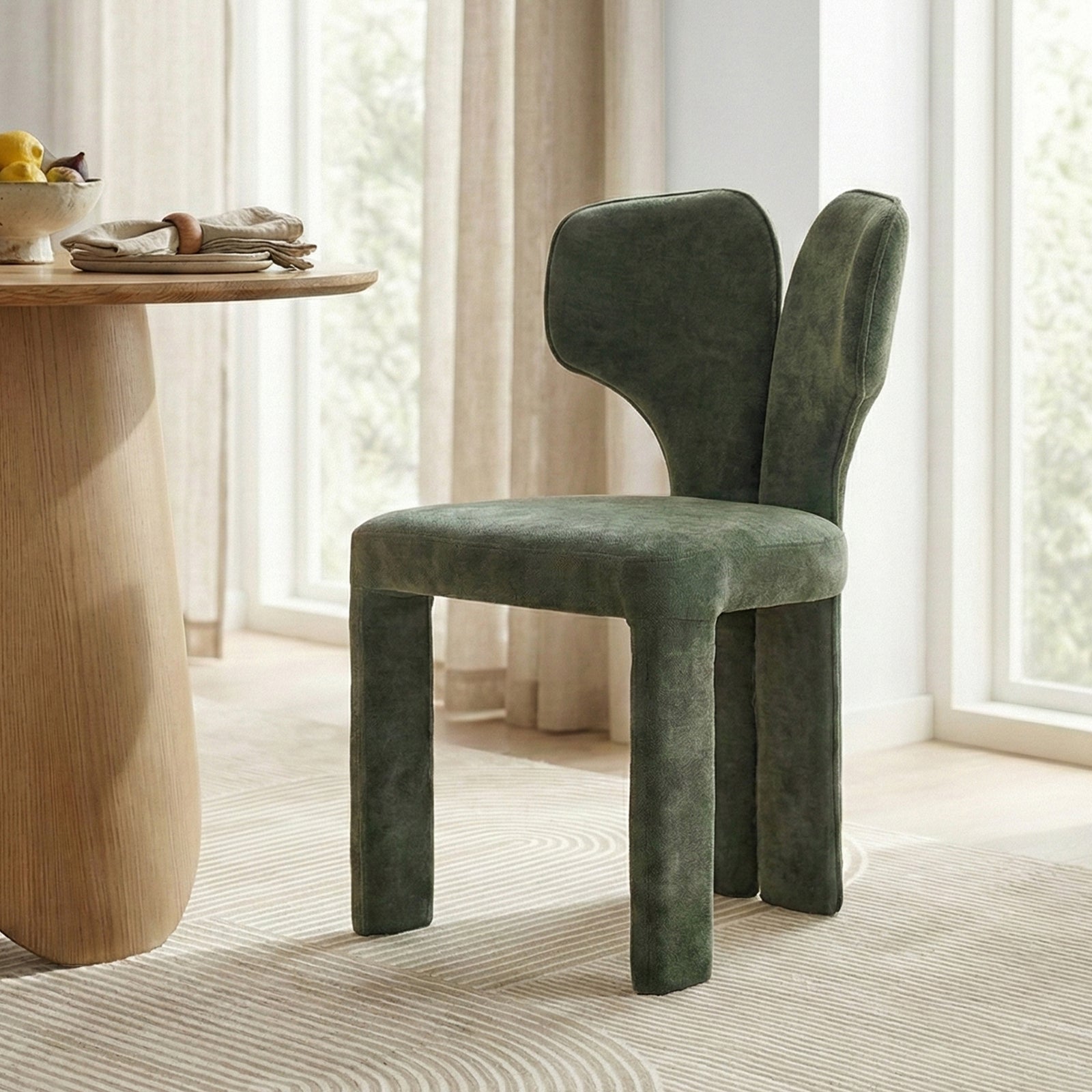 Green upholstered chair beside wooden table with fruit in bright room