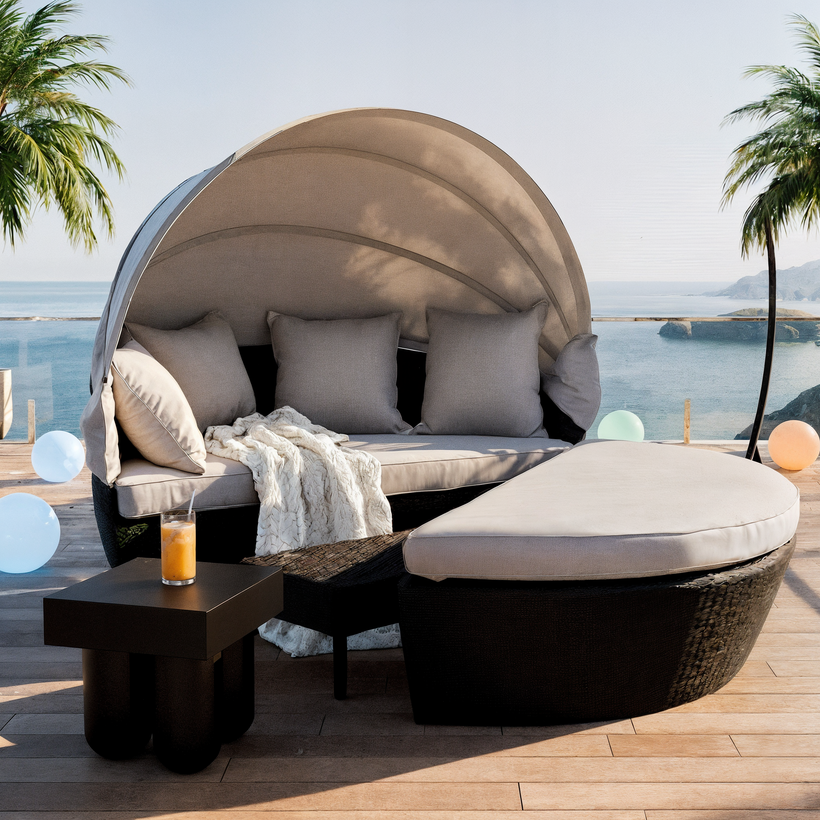 Outdoor patio setup featuring a beige cushioned corner sofa, a hanging wicker egg chair with a cream throw blanket, and a wooden coffee table with decorative vases. A stone side table holds a small plant and sculpture, set against a white stucco wall with a light blue shutter window and a potted plant in the background
