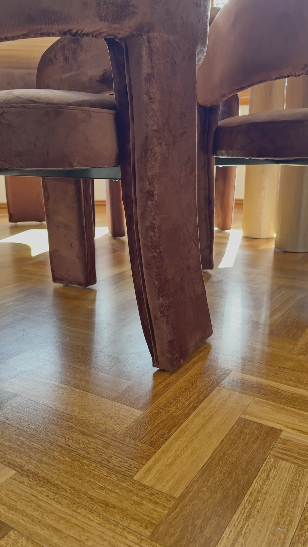 
A slow, cinematic close-up of a modern living room armchair with a unique open-back design. The chair has rounded, curved arms and is upholstered in a plush, rust-colored, velvety fabric. The camera moves down to the chair's base, showing its unique, curved feet. The shot highlights the chair's soft texture and elegant, contemporary form.